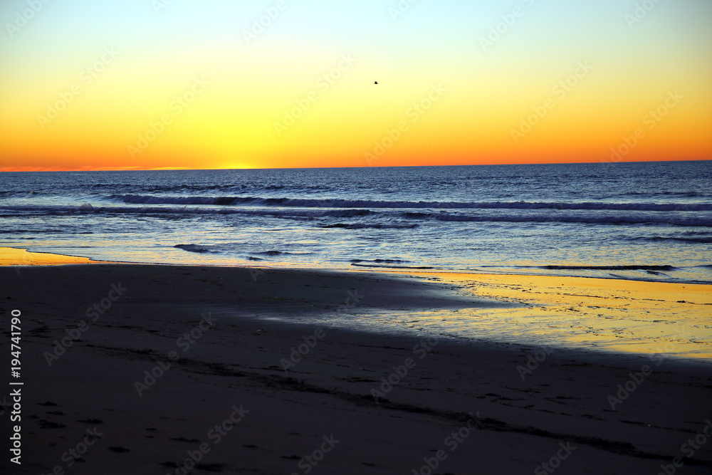 Vibrant orange and yellow sunset as seen from sandy beach on calm day along Pacific Ocean coast