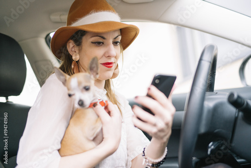 Beautiful young woman using her mobile phone in the car, With chihuhua dog