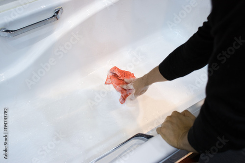 The hand cleans the white bath with a cloth and detergent