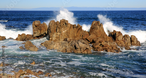 White waves crash against rugged rocks in Monterey, California's coastline