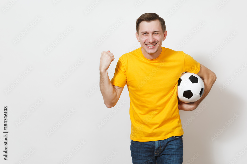 Inspired young European man, fan or player in yellow uniform hold soccer ball, doing winner gesture cheer favorite football team isolated on white background. Sport football healthy lifestyle concept.