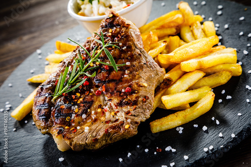 Grilled steak with french fries and vegetables served on black stone on wooden table 