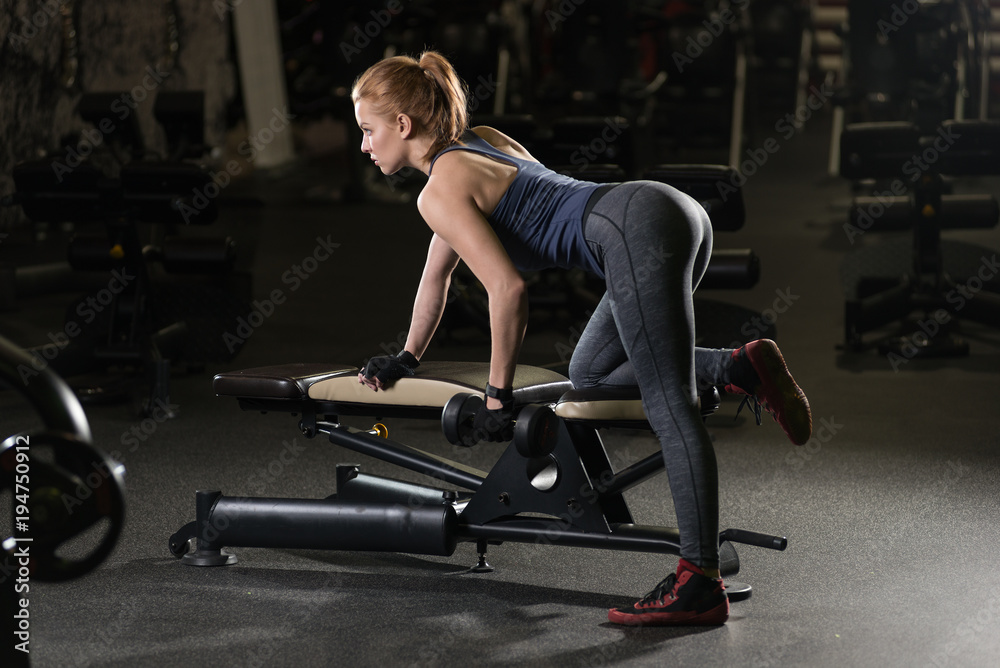 Beautiful sporty woman doing power fitness exercise at sport gym. Girl with dumbbell on black. Beautiful sporty woman doing power fitness exercise at sport gym. Girl with dumbbell on black.