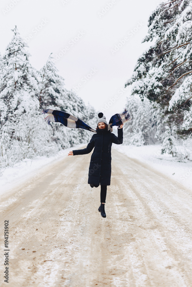 Stylish girl walking in the middle of a road on a snowy forest