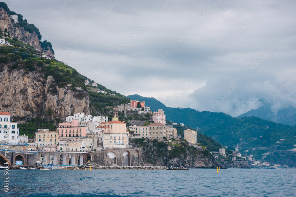 Panoramic aerial view shot of Amalfi village with the tiny beach coastline and colorful houses, located on the rock, Amalfi coast, Sorrento, Italy with blue mountains at background