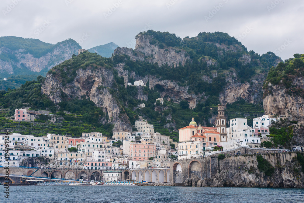 Panoramic aerial view shot of Amalfi village with the tiny beach coastline and colorful houses, located on the rock, Amalfi coast, Sorrento, Italy with blue mountains at background