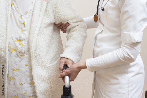 Obraz na płótnie Dłonie lekarki pomagającej i asekurującej starą kobietę i dłoń starej kobiety trzymającej uchwyt chodzika rehabilitacyjnego . w salonie