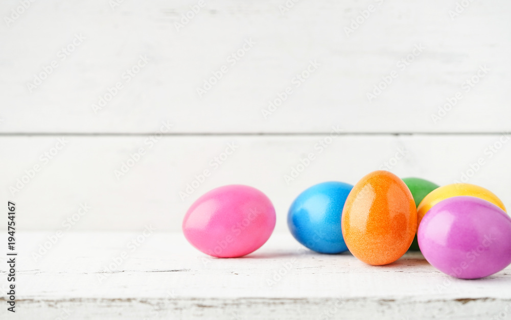 Obraz premium Bunte Ostereier vor weißem Holzhintergrund