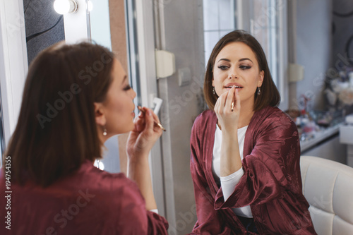 Young woman applying lipstick at home