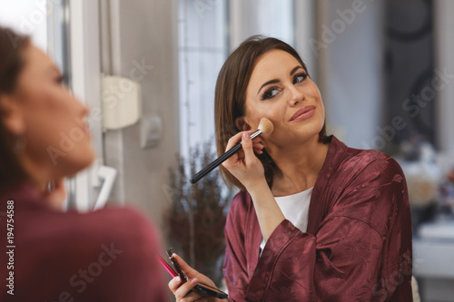 Young woman applying makeup on face at home