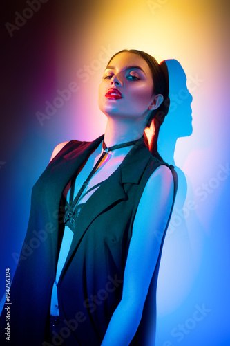 Sexy young brunette girl in black clothes, fashion accessories posing in studio over colorful background
