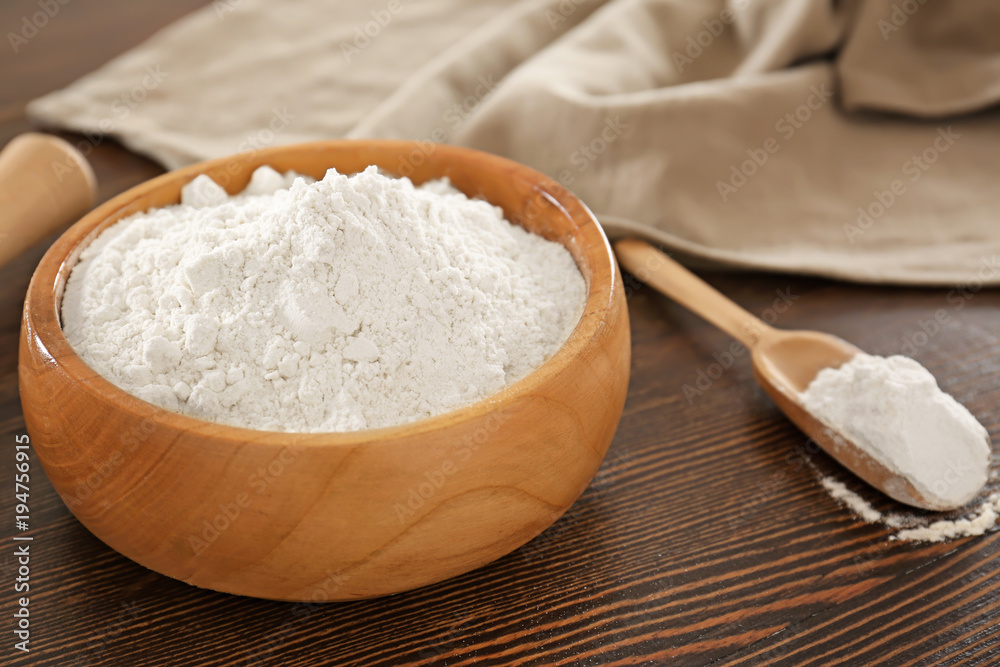 Bowl and scoop with wheat flour on wooden table Bowl and scoop with wheat flour on wooden table