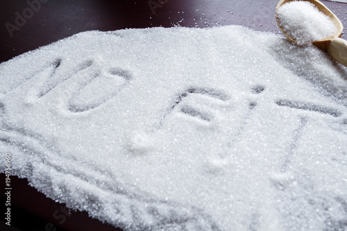 the word NO FIT written on a covered sugar and a wooden spoon on the table. photo