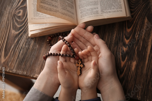 Photo Religious Christian girl with her mother holding rosary beads at table, closeup