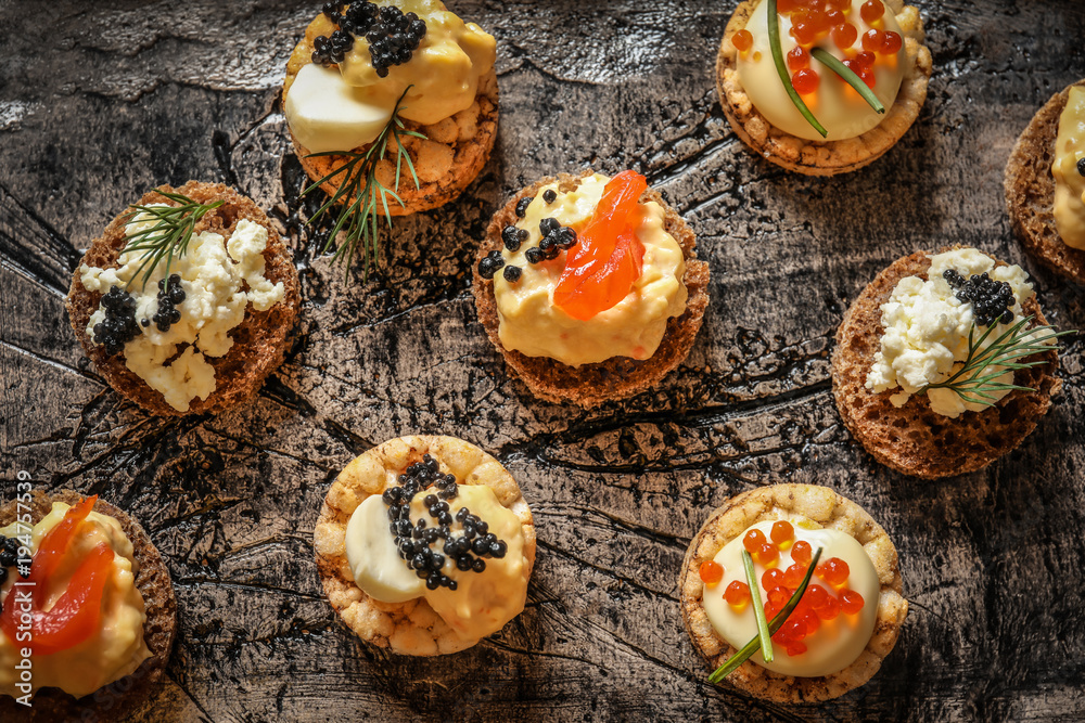 Delicious canapes with black and red caviar on textured background