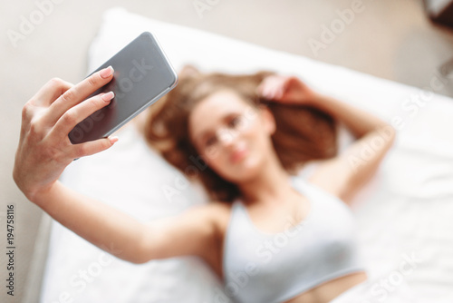 Attractive woman lies in bed and makes selfie