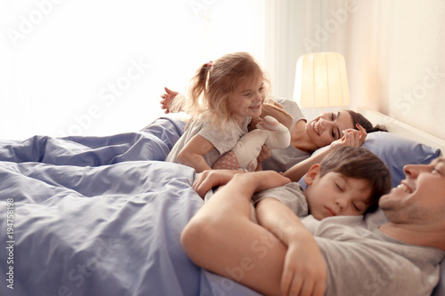 Cute awaken girl playing near sleeping family on bed at home