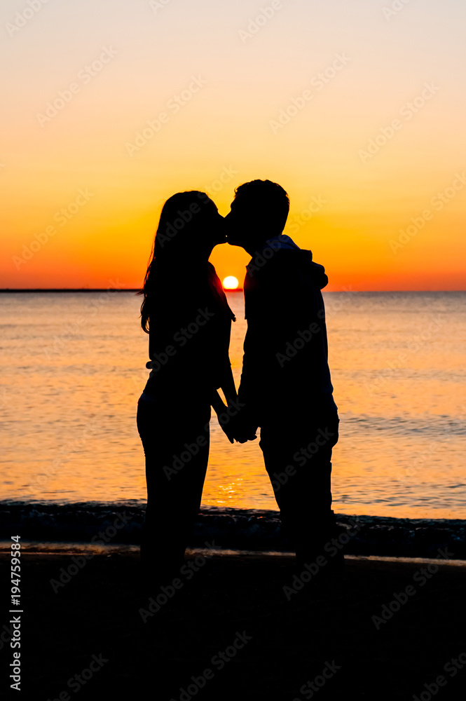 Silhouette of couple on the beach kissing at sunrise.