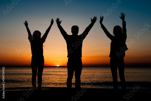 Silhouette of three friends in the morning at the beach looking at sunrise . Support, together, winning, helping, freedom concept.