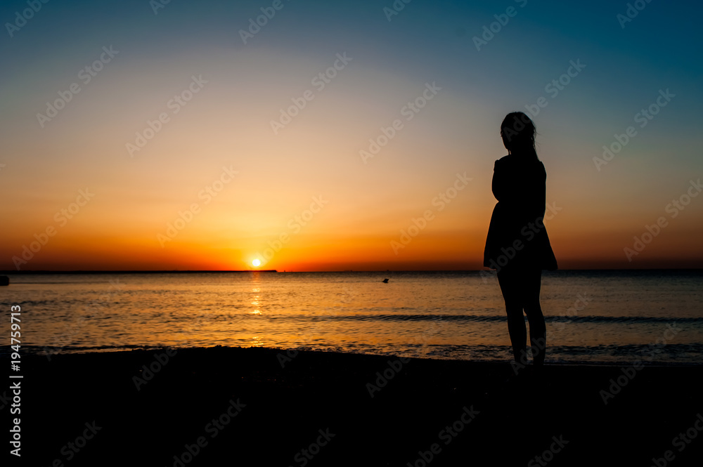Woman in summer dress standing on a sandy beach and looking to the sun