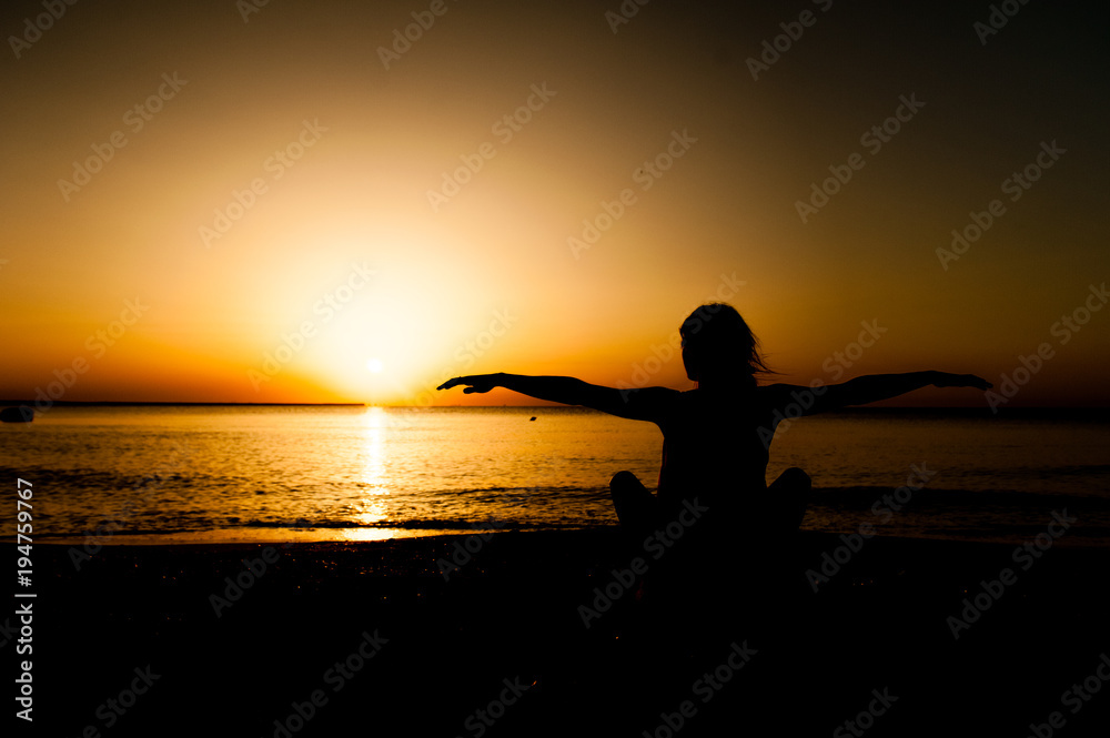 Silhouette young woman practicing yoga on the beach at sunrise.