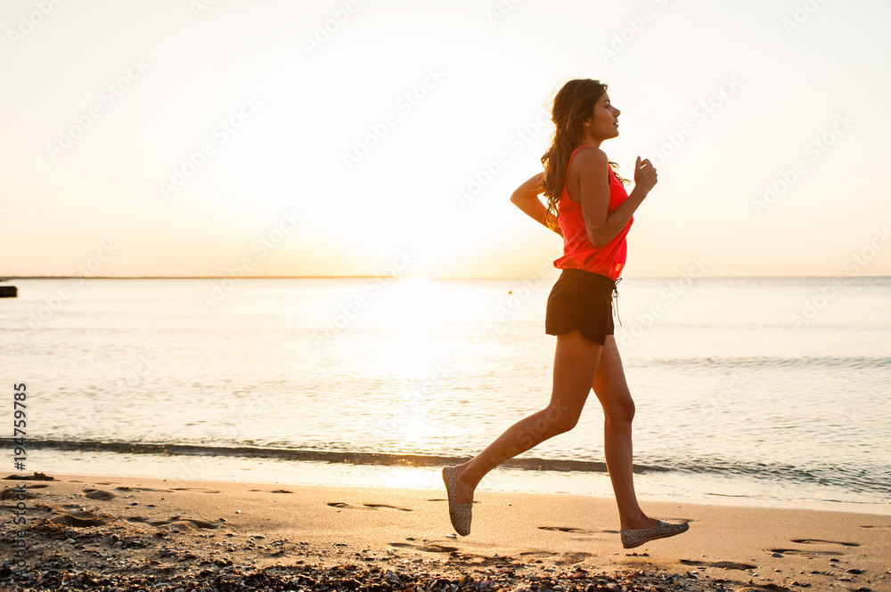 Woman running on beach during work out training. Fit beautiful young female model jogging at sunrise Woman running on beach during work out training. Fit beautiful young female model jogging at sunrise