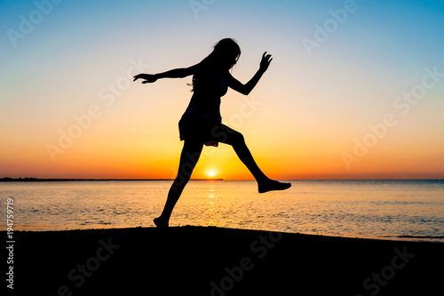 Silhouette of woman jumping in the air on the beach at sunrise.
