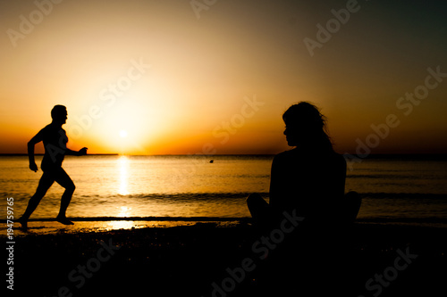 Silhouette young woman practicing yoga on the beach at sunrise.