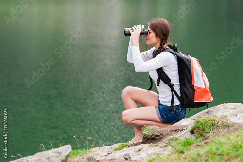 Canvas Print Young woman admiring the beautiful view of the lake and mountains, holding a binocular