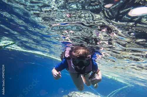 A teenager under the water in a mask and a tube with a phone