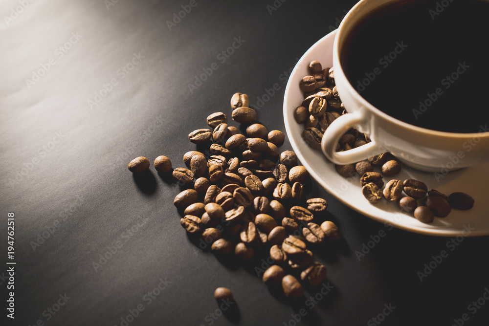 Fototapeta premium coffee is poured into a white cup with roasted coffee beans scattered on a black surface table