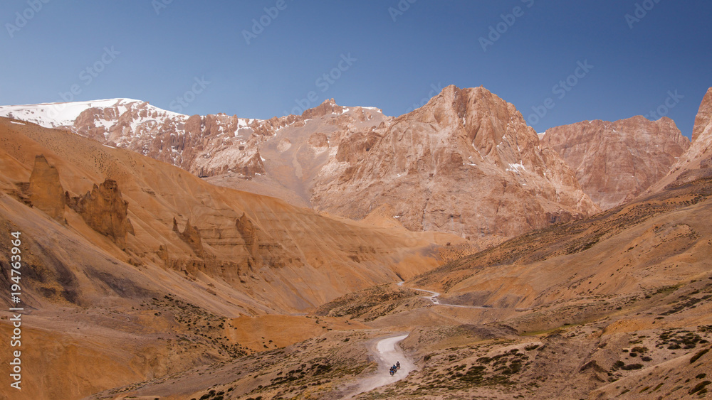 Bike trip through curly road along the river on himalaya highlands. Scenic view on landscape with golden  mountains, highway and three driving bikers. Region Ladakh. India. State Jammu and Kashmir.