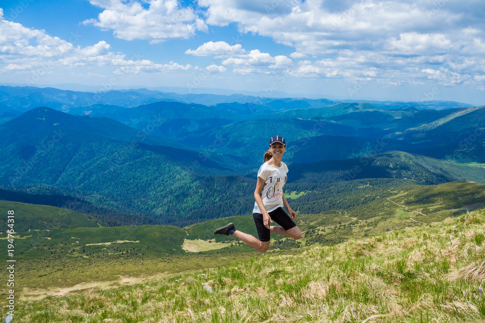 Young happy woman on the top of the hill enjoy beautiful view of sky and mountains, freedom and harmony concept