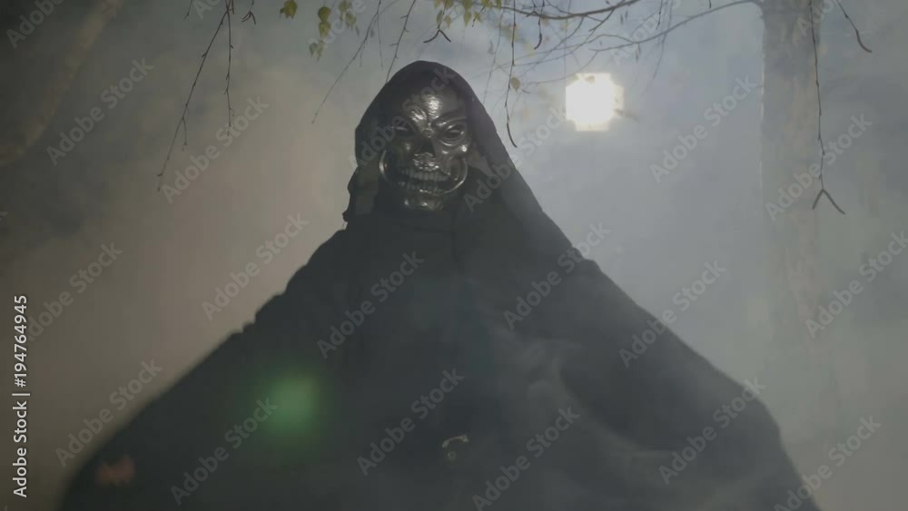Halloween movie scene with an adult wearing a skelton mask and mantle frightening the camera in a foggy forest