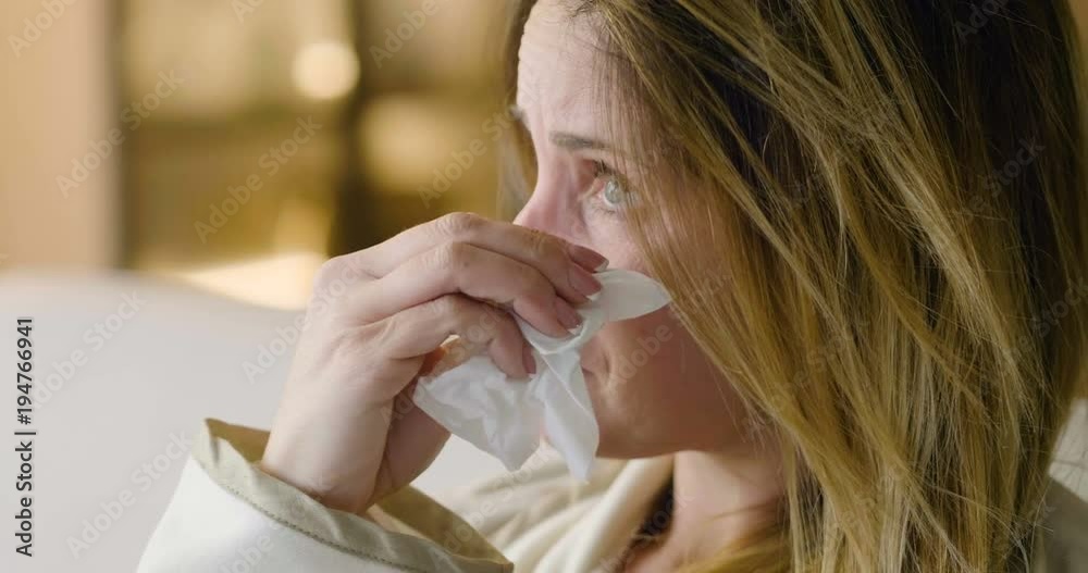 A woman sitting on the sofa in her house, cries desperately hugging the pillow and using the handkerchiefs to wipe away the tears. Concept of: despair, broken love, drama.