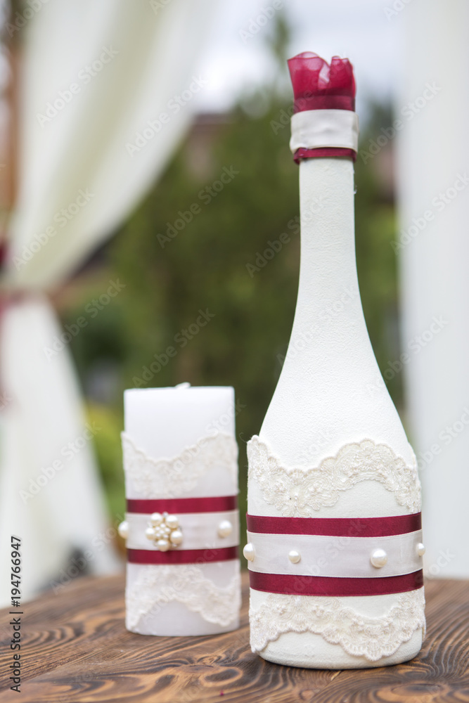 Set of wedding candle and bottle with wine color flowers and ribbon on a wooden surface (table). Outdoors. Copy space