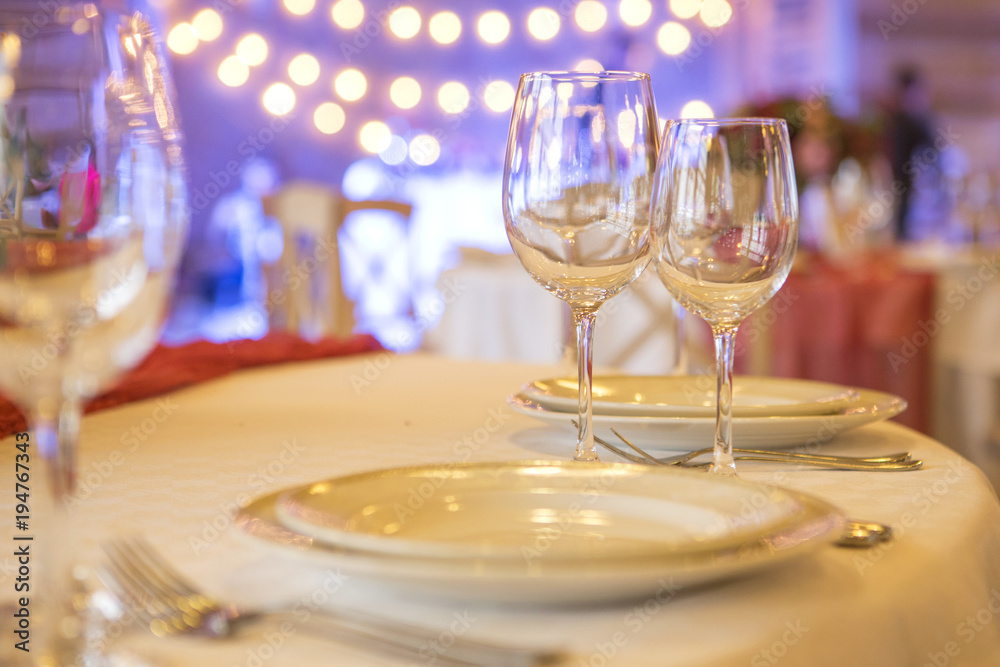 Set of glassess and plates on a wedding table surrounded by light garland and wine color flowers and tablecloth. Interior. Copy space