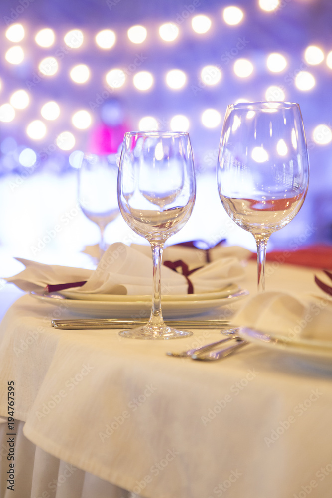 Set of glassess and plates on a wedding table surrounded by light garland and wine color flowers and tablecloth. Interior. Copy space Set of glassess and plates on a wedding table surrounded by light garland and wine color flowers and tablecloth. Interior. Copy space