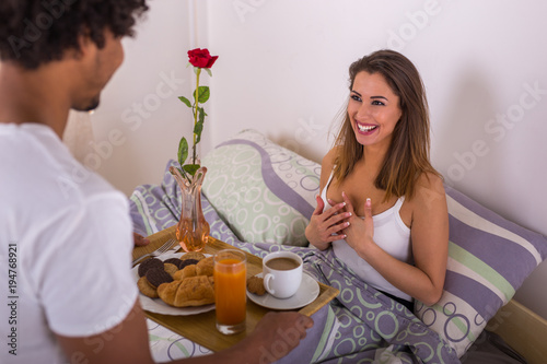 Handsome young man bringing breakfast into girlfriends bed