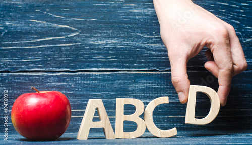 Red apple and letters ABCD. The hand puts the letter D in the alphabet order. Apple for the teacher. The concept of teaching and education. School, college, kindergarten, university.  photo