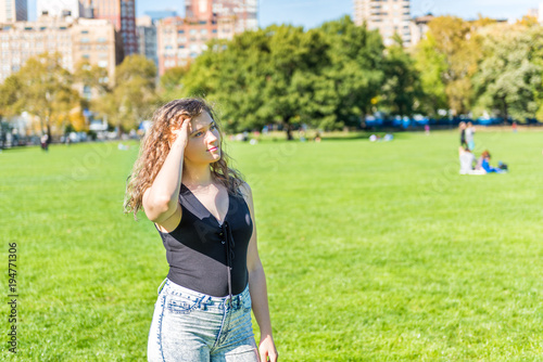 Closeup of one happy young woman hipster millennial touching hair with hand, arm in Central Park in New York City nyc during sunny autumn day with modern skyscrapers buildings and people