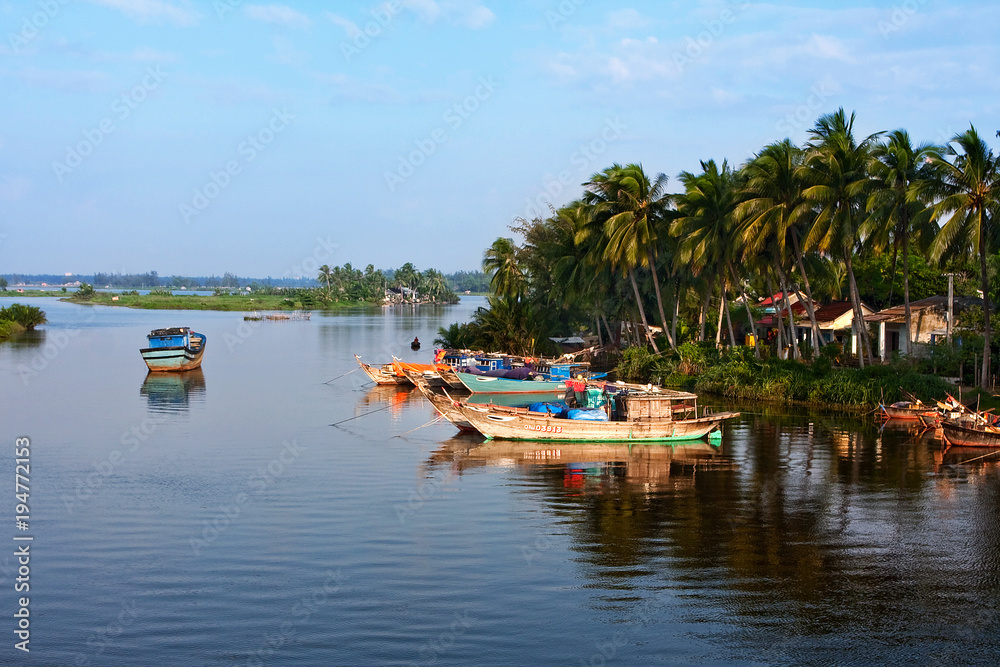 a fishing boat on the background of a colorful beautiful dawn. Hoian. Vietnam. Paradise rest. Relax. Reflections in the water, river bank, silhouettes of palm trees.