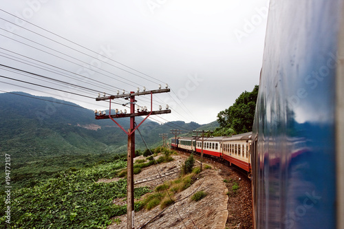 The train rides by rail through the jungle in Vietnam. The long train of many carriages. Rails and sleepers, poles along the roads. To travel around the country. The trip from Hanoi to Ho Chi Minh.