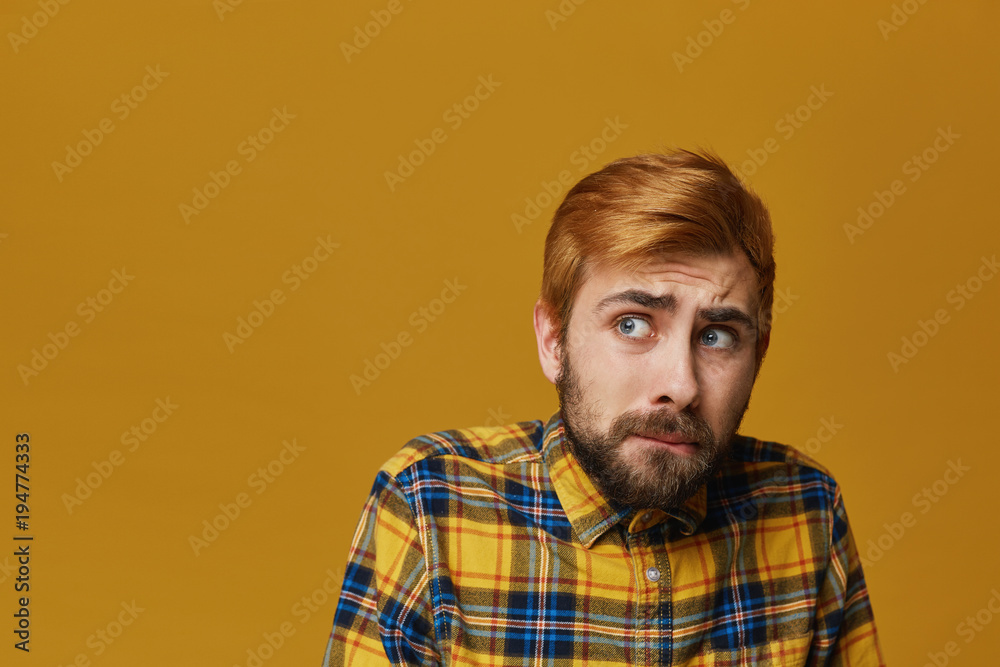 Scarried and worried guy looking aside and afraid about something. Unshaved wears yellow plaid shirt. isolated over yellow background. Facial expression.