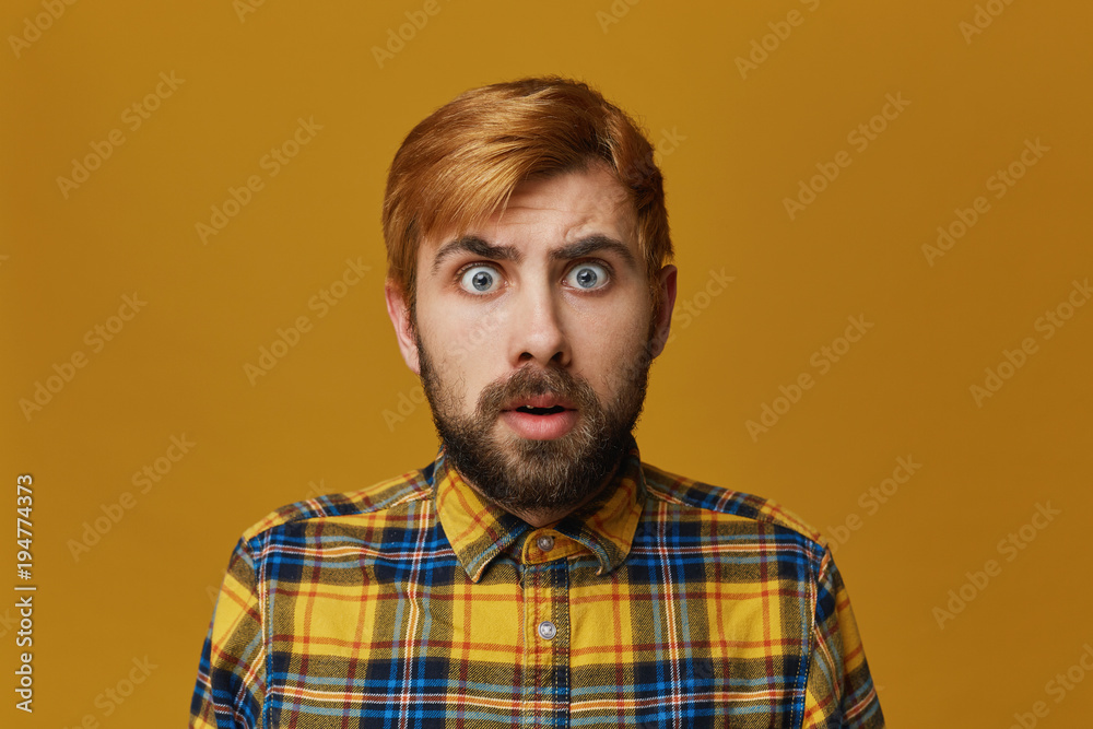 Portrait of stupefied bearded male, with dyed blond gold hair keeps mouth widely opened, wonders about something, isolated over yellow background. Facial expression Portrait of stupefied bearded male, with dyed blond gold hair keeps mouth widely opened, wonders about something, isolated over yellow background. Facial expression