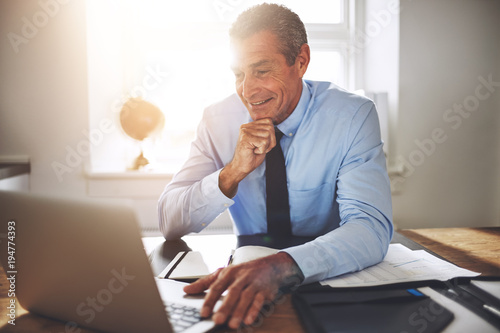 Smiling mature businessman working online at his office desk photo