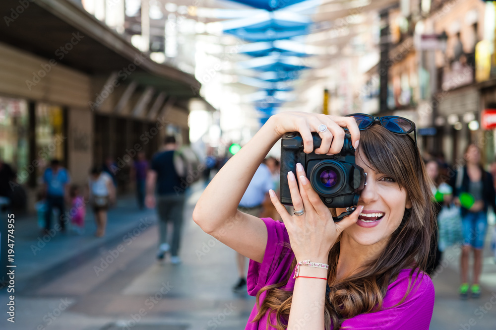 Young woman tourist holding a photo camera and taking picture in Plaza del Sol square, Madrid, Spain.