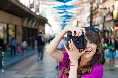 Young woman tourist holding a photo camera and taking picture in Plaza del Sol square, Madrid, Spain. © vladteodor