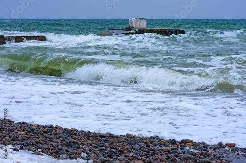 Stormy day at winter beach. Icy waves breaking at snow covered rocks. March 02, 2018. Black sea, Odessa, Ukraine photo