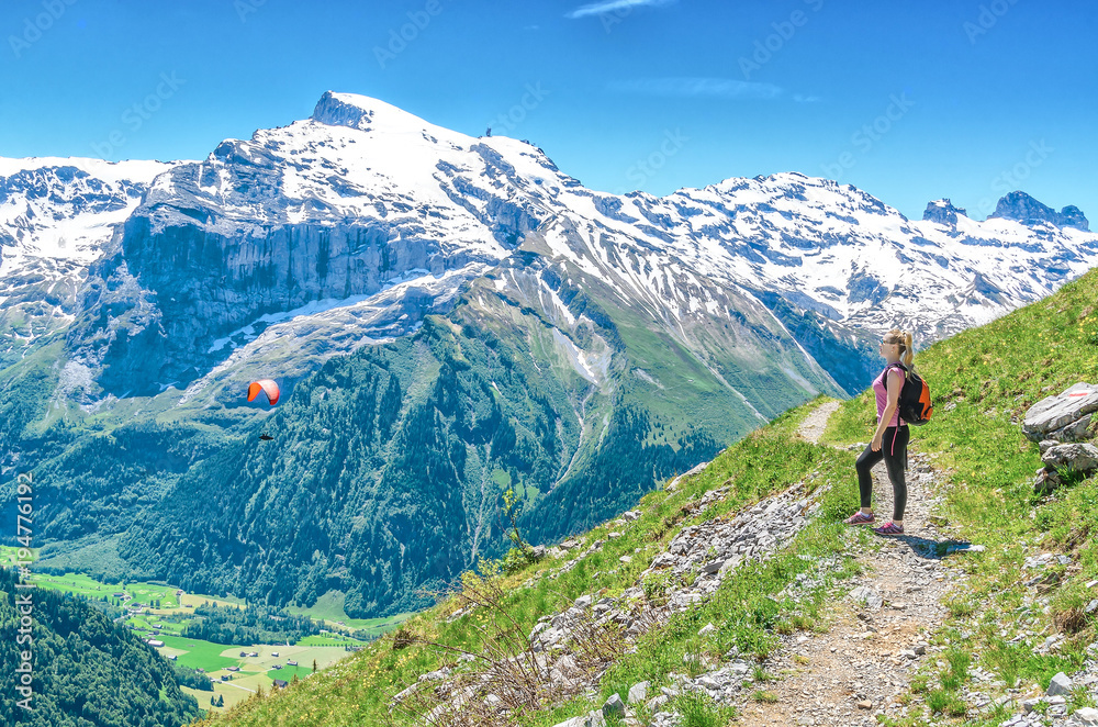 A girl with a red backpack admiring the scenery of the Alpine mountains. Landscape of the Swiss Alps, the Engelberg resort.